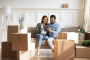 A happy couple sits on a sofa amidst many cardboard packing boxes