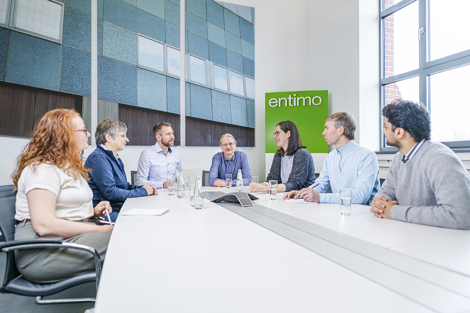 A group of colleagues in a bright meeting room sitting around a large white table.