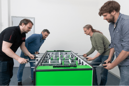 Four members of entimo's team taking a break and playing a round of what the Germans call kicker, North Americans call foosball, and otherwise known as table football.